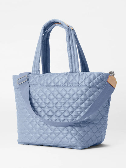 The MZ Wallace Medium Metro Tote Deluxe in Stone Blue Oxford features dual handles, a detachable shoulder strap, Italian leather trim, and a top zip closure, merging elegance with practicality.