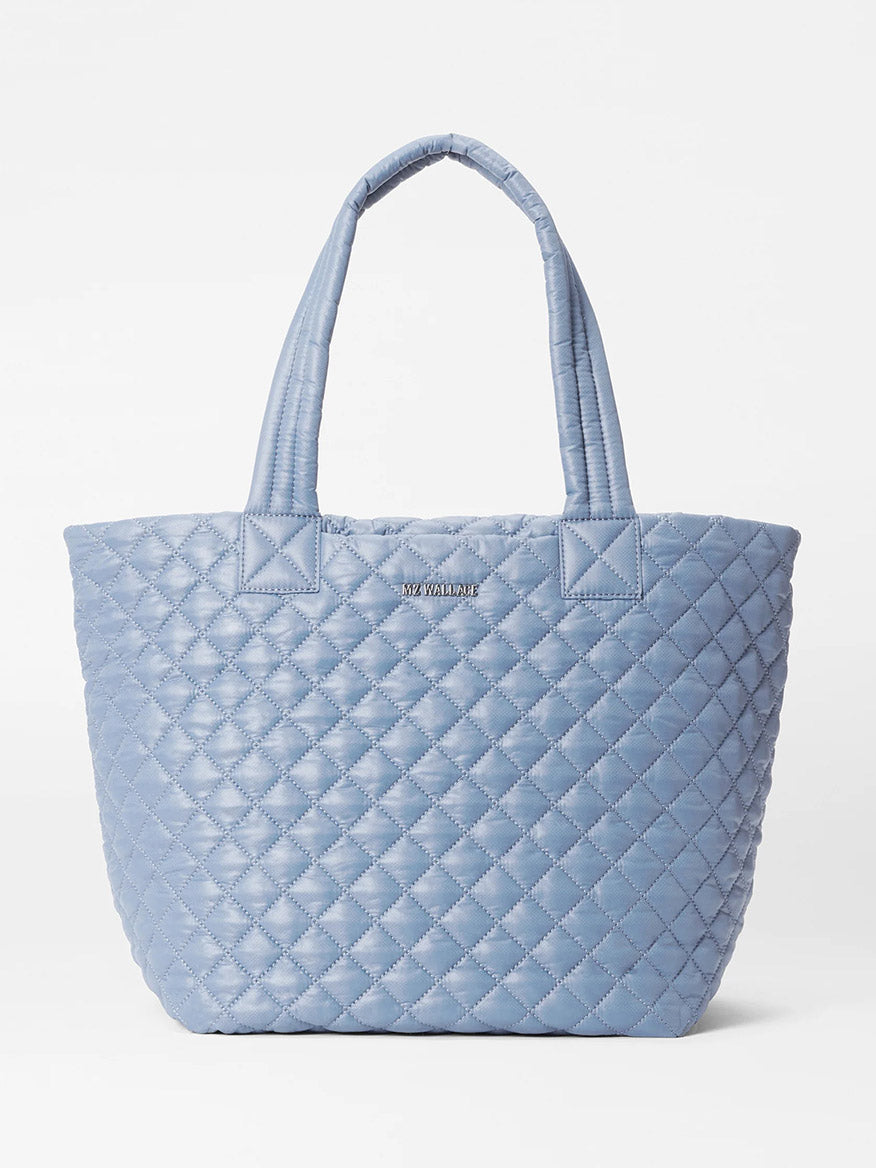 The MZ Wallace Medium Metro Tote Deluxe in Stone Blue Oxford features two handles and a subtle metallic logo, blending elegance with functionality for on-the-go organization.