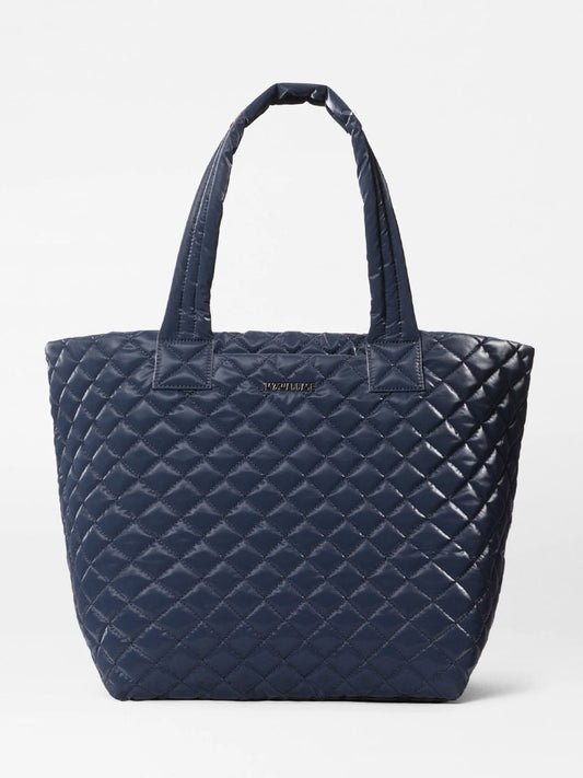 The MZ Wallace Medium Metro Tote Deluxe in Ink Liquid Oxford, featuring a quilted navy finish, two handles, and a small metallic logo on the front, is displayed against a plain white background.