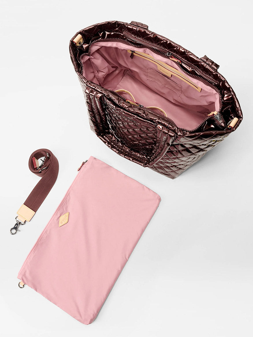 The MZ Wallace Medium Metro Tote Deluxe in Bordeaux Lacquer Oxford is displayed with a pink interior, detachable maroon strap, and a matching pink pouch beside it on a white surface.