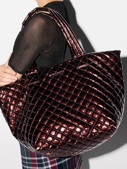 Person carrying an MZ Wallace Medium Metro Tote Deluxe in Bordeaux Lacquer Oxford, wearing a black top and plaid skirt.