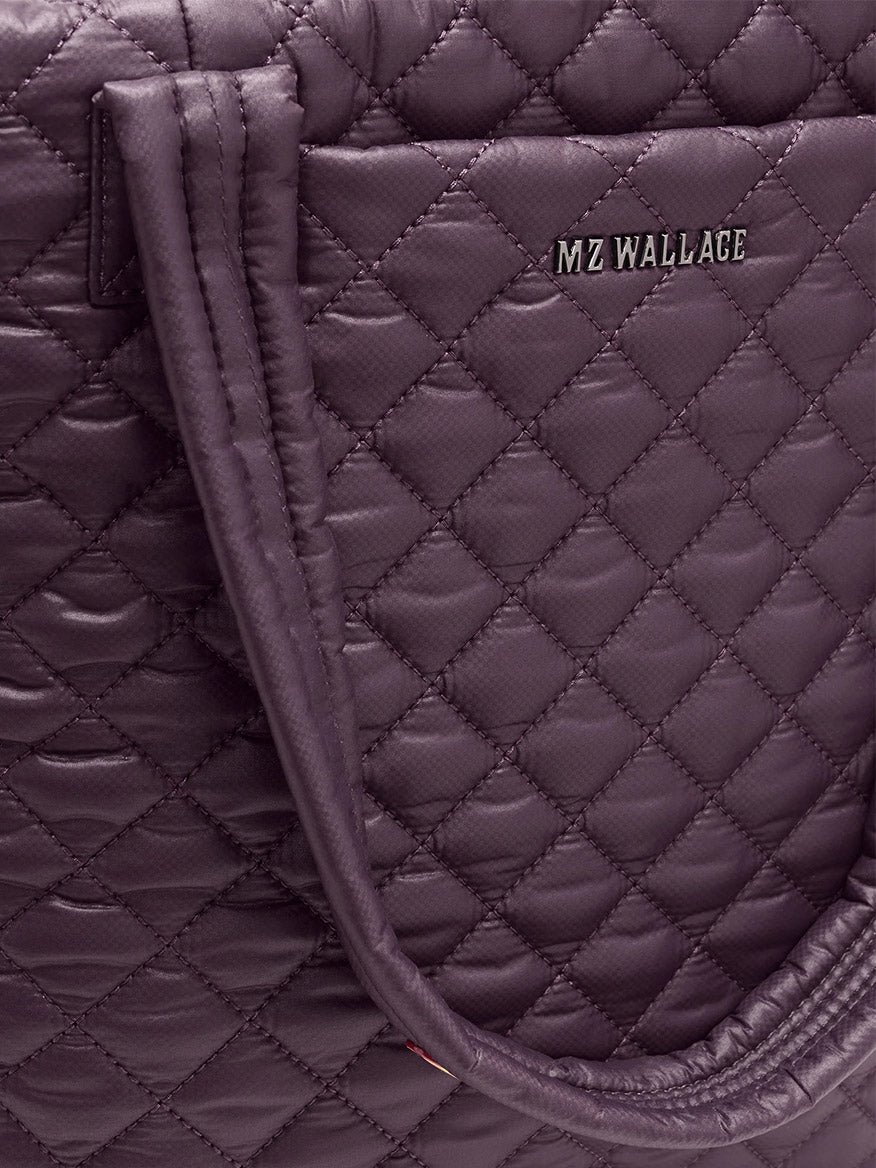 Close-up of the MZ Wallace Medium Metro Tote Deluxe in Raisin Oxford, featuring double handles, front "MZ WALLACE" branding, and a quilted featherlight design that highlights its chic style.