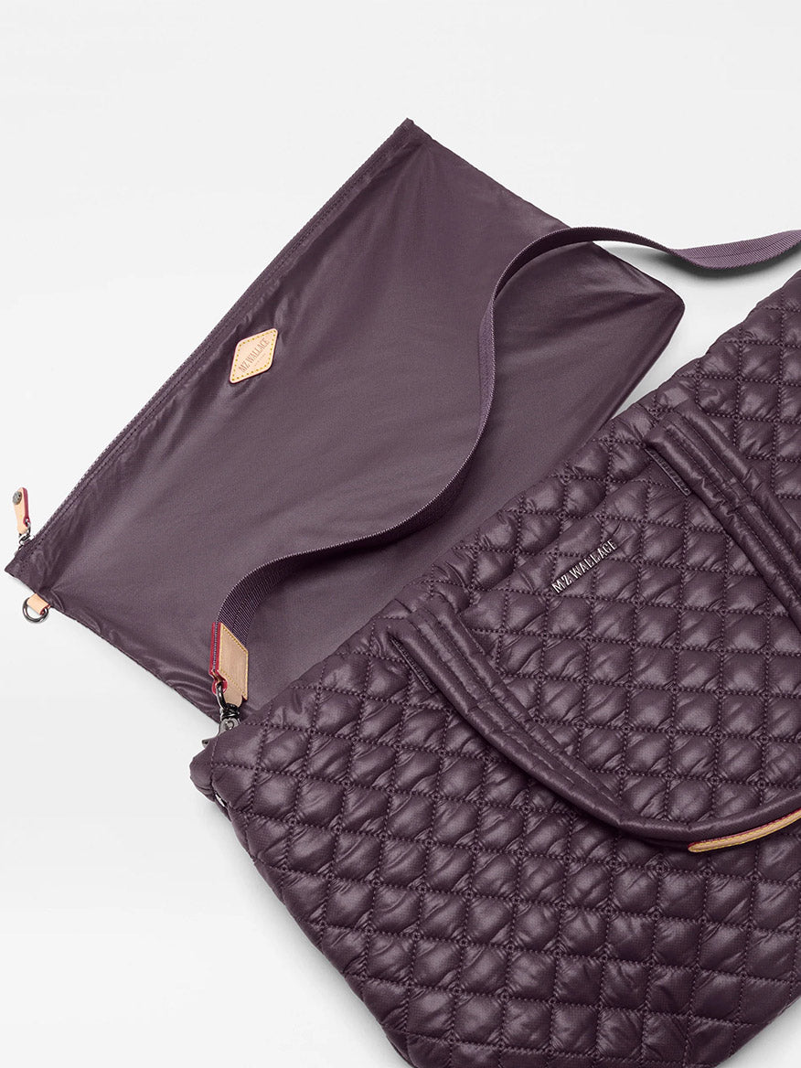 The MZ Wallace Medium Metro Tote Deluxe in Raisin Oxford features a quilted design, dual handles, an open flap revealing its spacious interior, and a matching strap—offering featherlight style and versatile function.