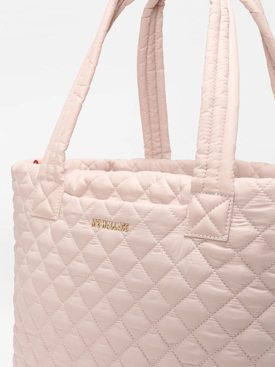 Close-up of the MZ Wallace Medium Metro Tote Deluxe in City Pink Oxford, showcasing its quilted design, short handles, gold "MZ WALLACE" lettering on the front, and a handy luggage sleeve.