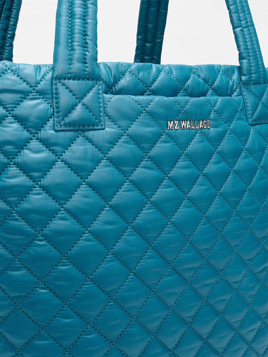 Close-up of the MZ Wallace Medium Metro Tote Deluxe in Pacific Oxford, a featherlight quilted bag with dual handles and a small metallic "MZ WALLACE" logo.
