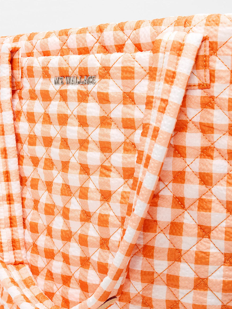 Close-up of the MZ Wallace Medium Metro Tote Deluxe in Sunset Orange Gingham Oxford, a quilted work and travel bag with logo detail, crafted from recycled Oxford nylon.