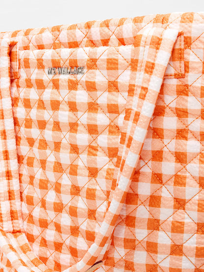 Close-up of the MZ Wallace Medium Metro Tote Deluxe in Sunset Orange Gingham Oxford, a quilted work and travel bag with logo detail, crafted from recycled Oxford nylon.