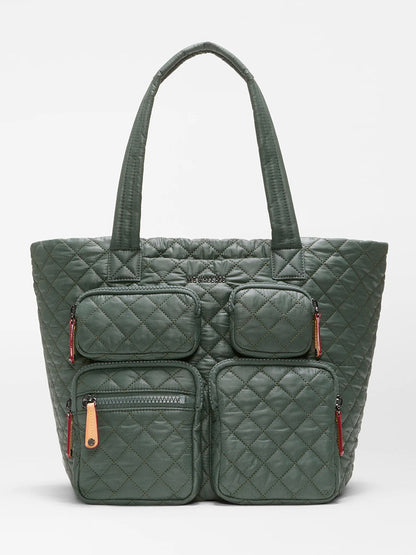 Introducing the MZ Wallace Medium Metro Travel Tote in Juniper Oxford, a dark green quilted travel bag crafted from recycled Oxford nylon. It features two long handles and four exterior zippered pockets on the front, combining eco-friendly materials with stylish design for your travels.