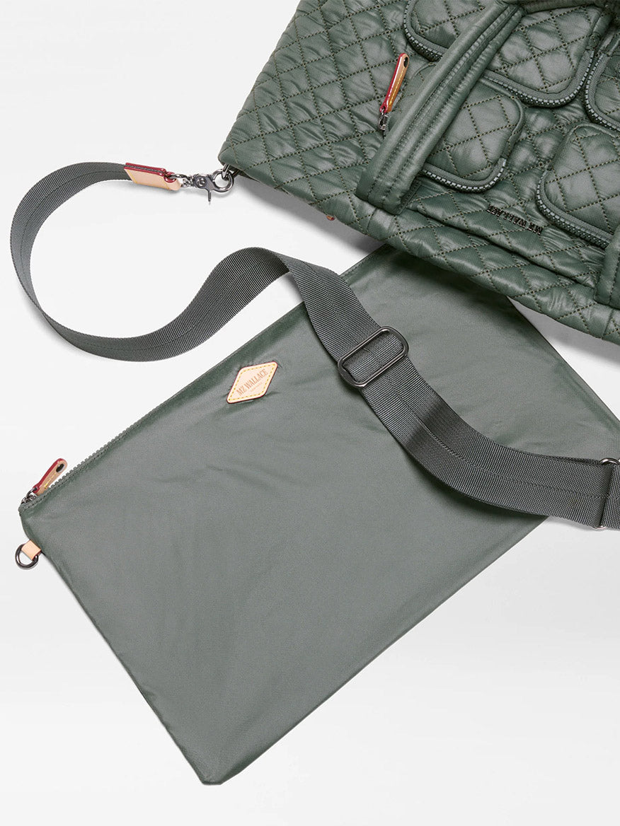 The MZ Wallace Medium Metro Travel Tote in Juniper Oxford, featuring a green quilted design and visible zippers, is placed beside a matching flat pouch with a shoulder strap on a white surface.