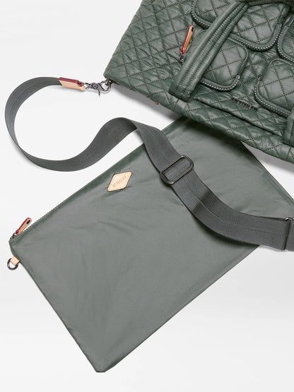 The MZ Wallace Medium Metro Travel Tote in Juniper Oxford, featuring a green quilted design and visible zippers, is placed beside a matching flat pouch with a shoulder strap on a white surface.