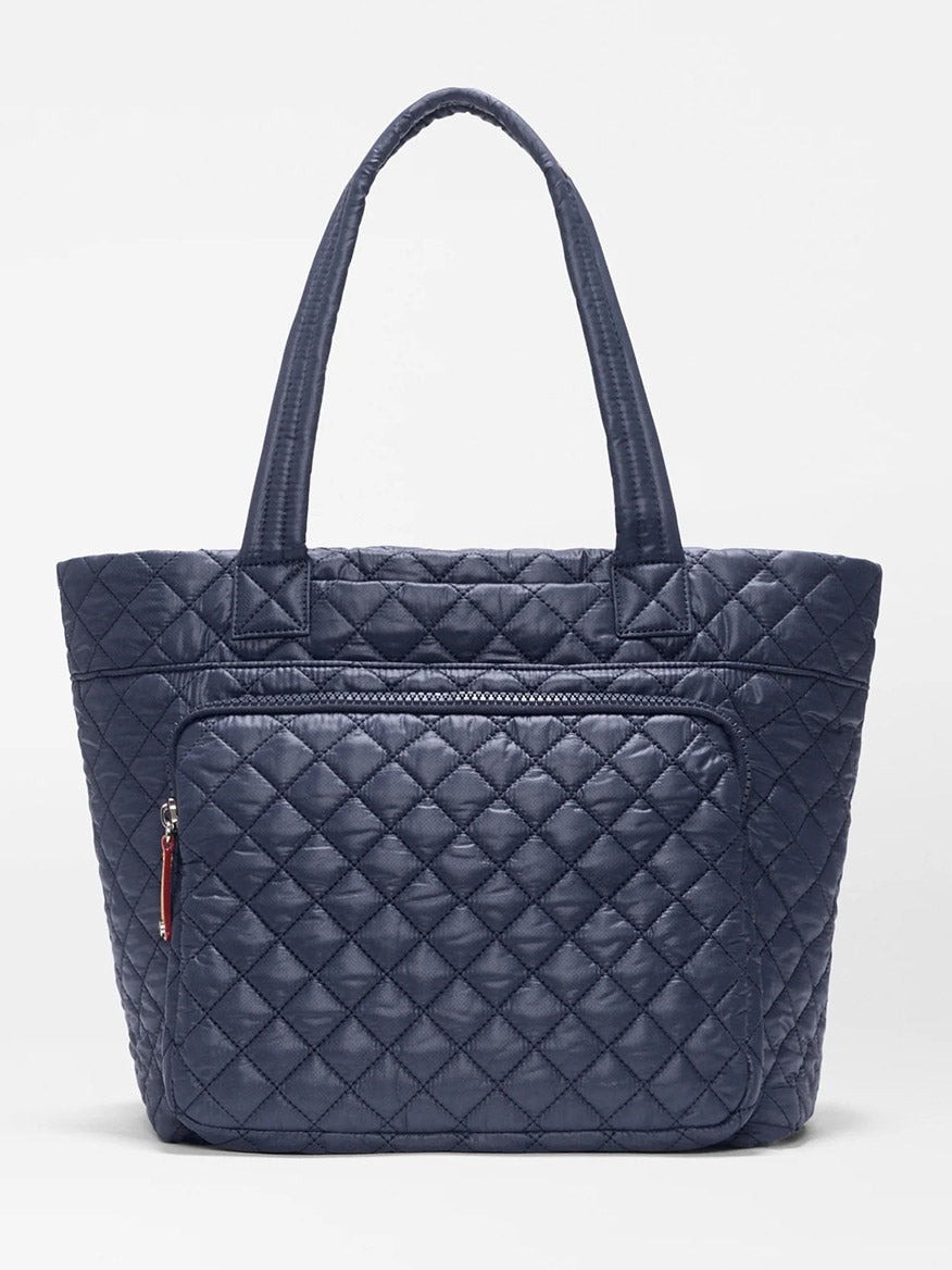 The MZ Wallace Medium Metro Travel Tote in Dawn Oxford is a navy blue quilted bag made from recycled nylon, featuring two handles and a front zippered pocket, shown against a plain white background.