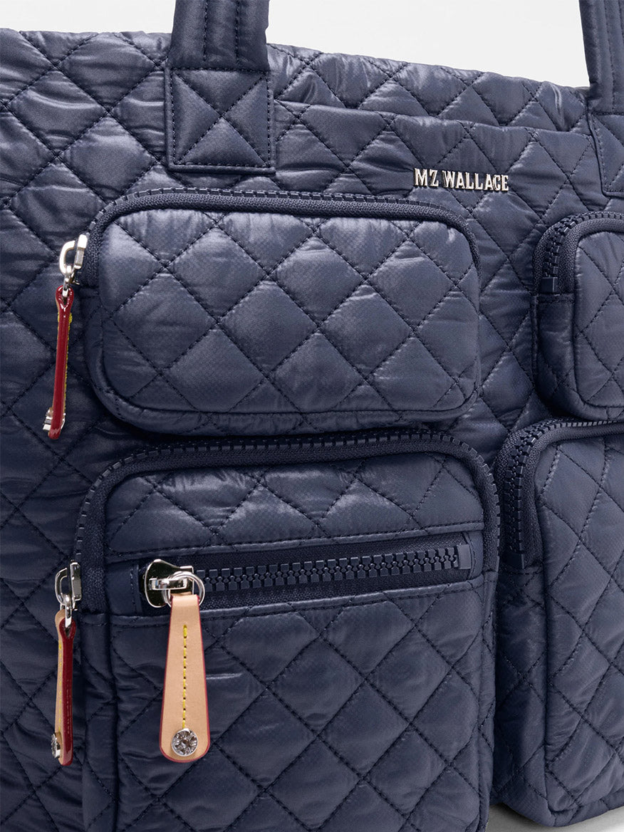 Close-up of the MZ Wallace Medium Metro Travel Tote in Dawn Oxford, a navy blue quilted bag crafted from recycled nylon with three zippered pockets, leather pulls, and silver hardware—ideal for use as a travel tote or laptop bag.