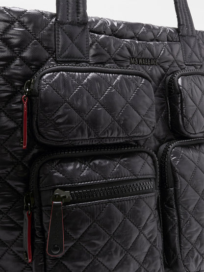 Close-up of the MZ Wallace Medium Metro Travel Tote in Black Oxford—a black quilted bag crafted from durable Black Oxford Nylon, featuring four front zippered pockets with red zipper pulls and a small MZ Wallace logo—making it an ideal choice for work and travel.