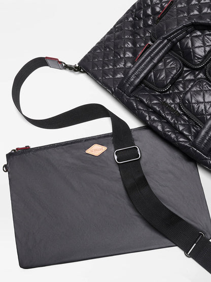 A MZ Wallace Medium Metro Travel Tote in Black Oxford with short handles is partially visible next to a flat black pouch featuring a shoulder strap and a small tan diamond-shaped logo tag.