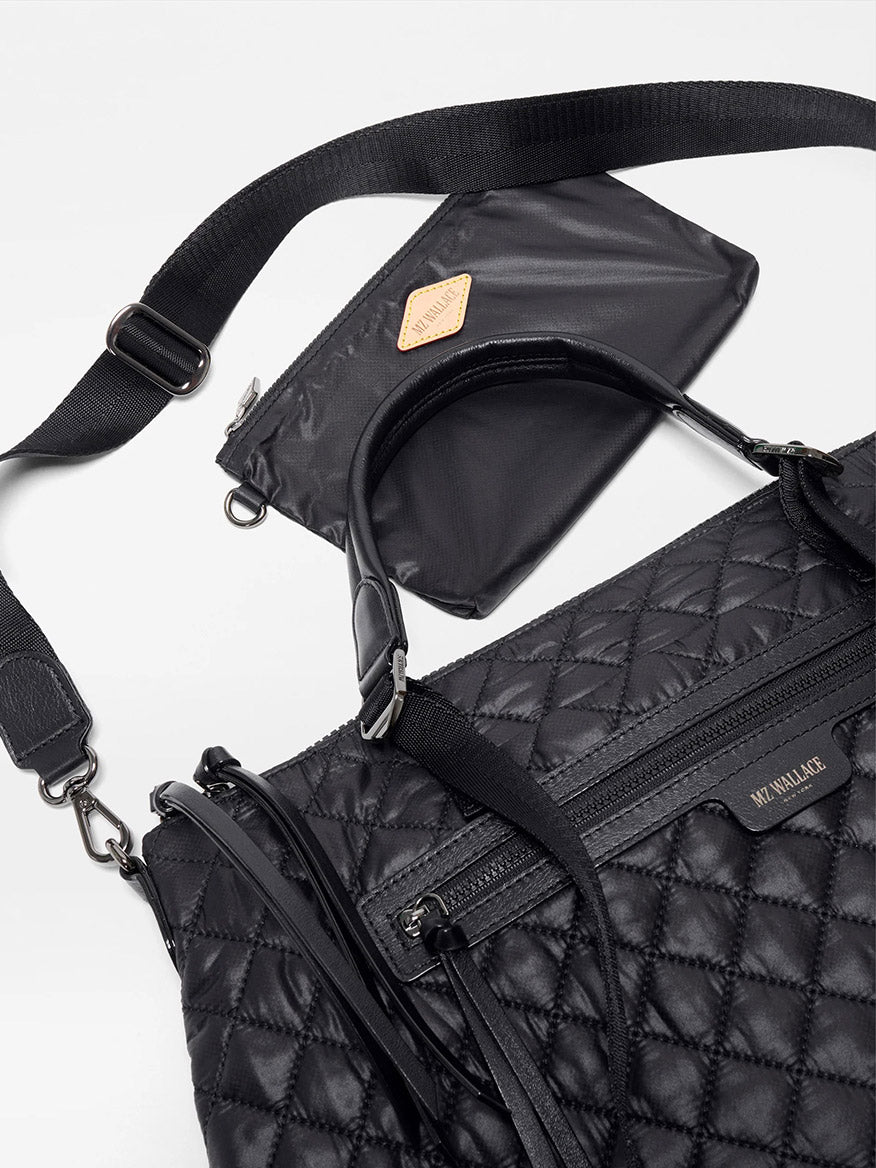 The MZ Wallace Medium Park Satchel in Black Oxford, featuring handles, a detachable strap, and quilting, is shown beside a small black zippered pouch with a brown label—an ideal everyday bag.