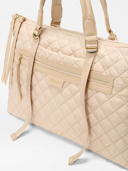 The MZ Wallace Medium Park Satchel in Buff Oxford features a beige quilted design with double handles, gold-tone hardware, and front zip pockets—an elegant everyday bag shown against a white background.