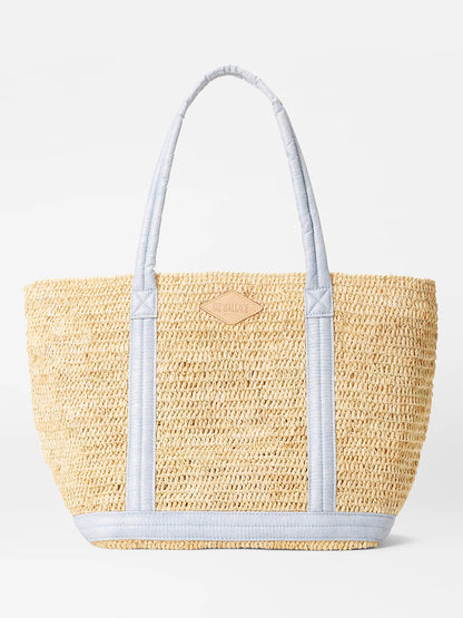 A MZ Wallace Medium Raffia Tote in Chambray/Raffia crafted from sustainably sourced Raffia features light blue fabric handles and trim, with a small leather patch embossed on the front.