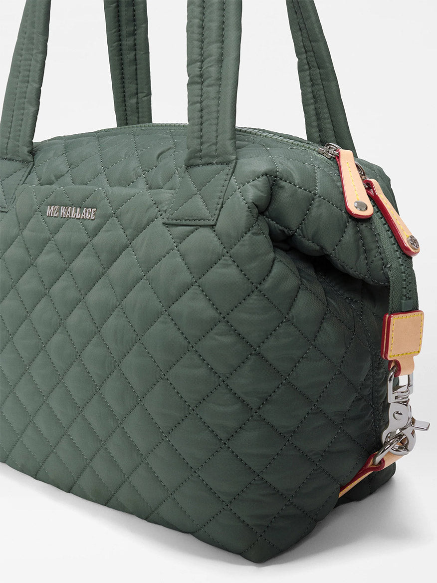 Introducing the MZ Wallace Medium Sutton Deluxe in Juniper Oxford—a green quilted handbag made from recycled Oxford nylon. It features double handles, a metal zipper, and the “MZ Wallace” name displayed on the front, seamlessly combining everyday versatility with style and sustainability.