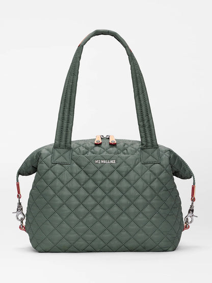 The MZ Wallace Medium Sutton Deluxe in Juniper Oxford is a green quilted handbag featuring two handles, a zip closure, and silver hardware. Crafted from recycled Oxford nylon for a structured carry, it is displayed against a plain white background.