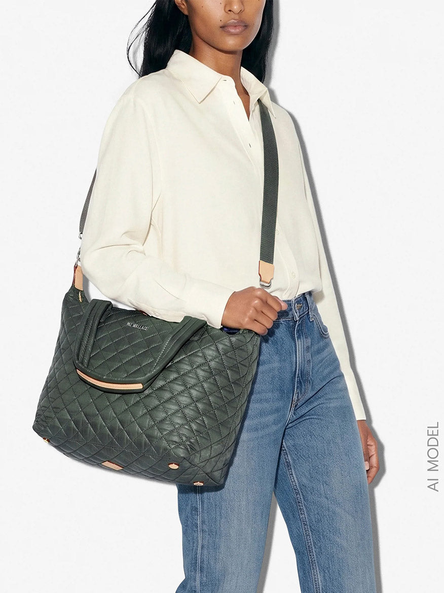 A woman in a white blouse and blue jeans carries the MZ Wallace Medium Sutton Deluxe in Juniper Oxford, a large quilted green shoulder bag crafted from recycled Oxford nylon for a stylish yet structured look.