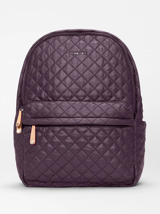The MZ Wallace Metro Backpack II in Raisin Oxford is a quilted dark purple backpack made from recycled nylon, featuring a front zip pocket, tan zipper pulls, and the "MZ WALLACE" logo—ideal as a stylish laptop backpack.