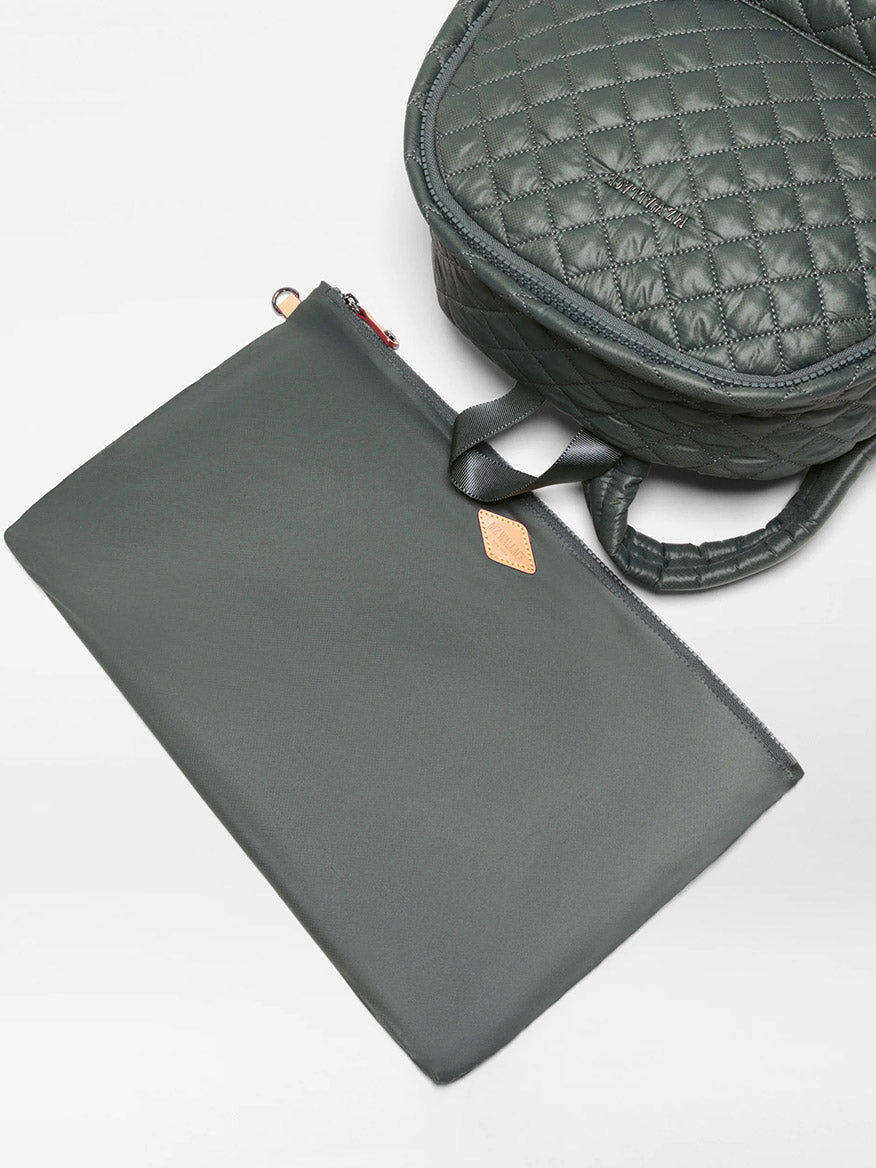 A quilted MZ Wallace Metro Backpack II in Juniper Oxford, crafted from recycled nylon, rests on a light surface beside a matching flat zippered pouch.