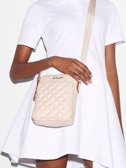 A person in a white dress holding a MZ Wallace Metro Crossbody in Mushroom Oxford with an adjustable nylon crossbody strap.