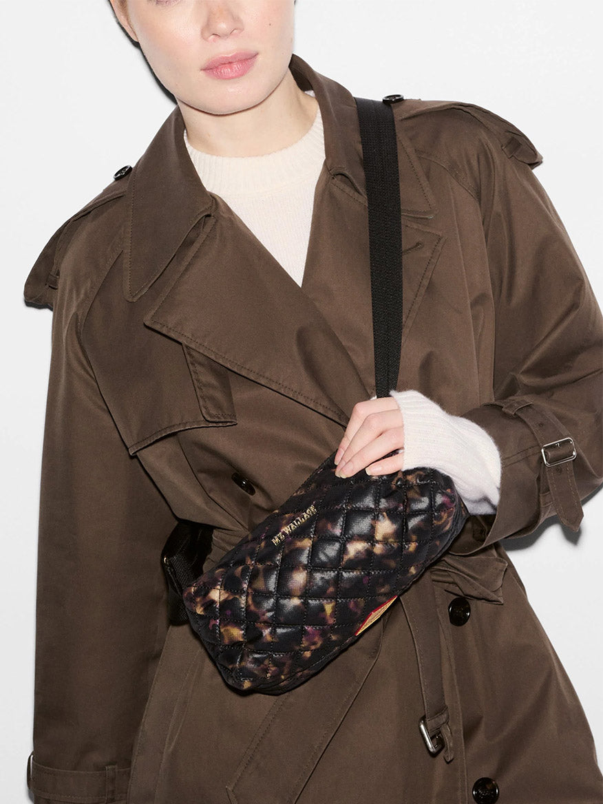 A person wearing an MZ Wallace Metro East West Crossbody in Tortoise Shell Oxford, a quilted black and brown tortoise-patterned recycled nylon bag with an adjustable strap.