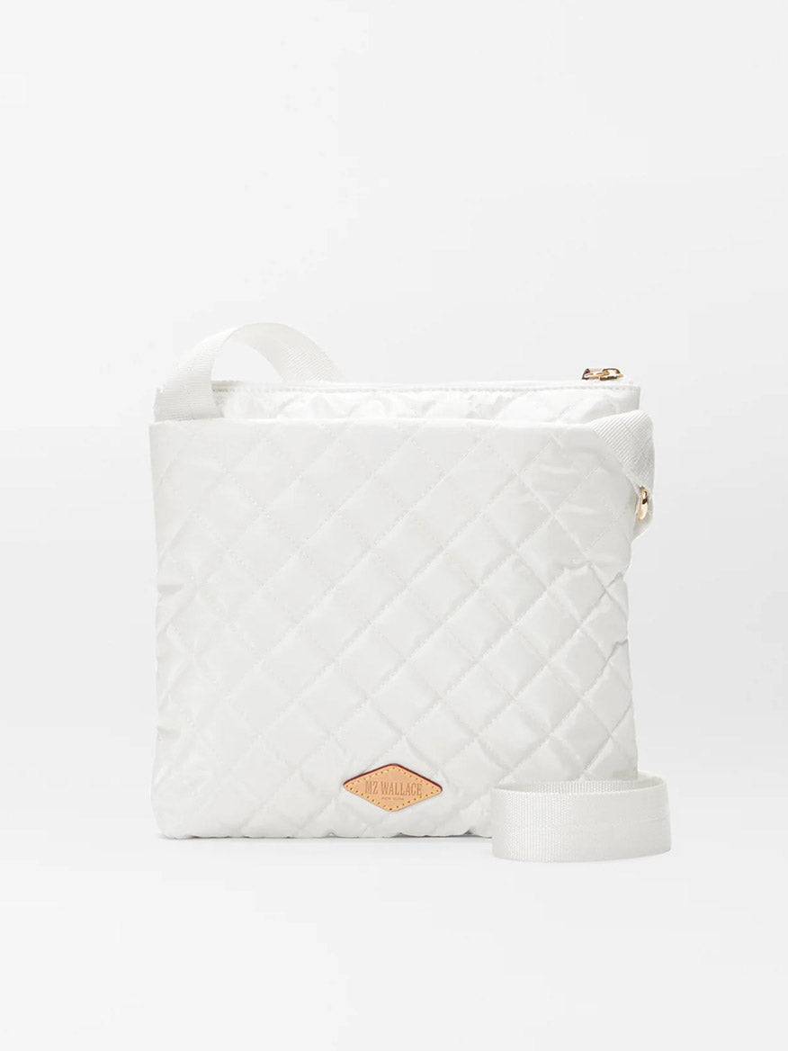 White MZ Wallace Metro Flat Crossbody in Pearl Metallic Oxford with a gold zipper and a branded label, displayed against a plain backdrop.