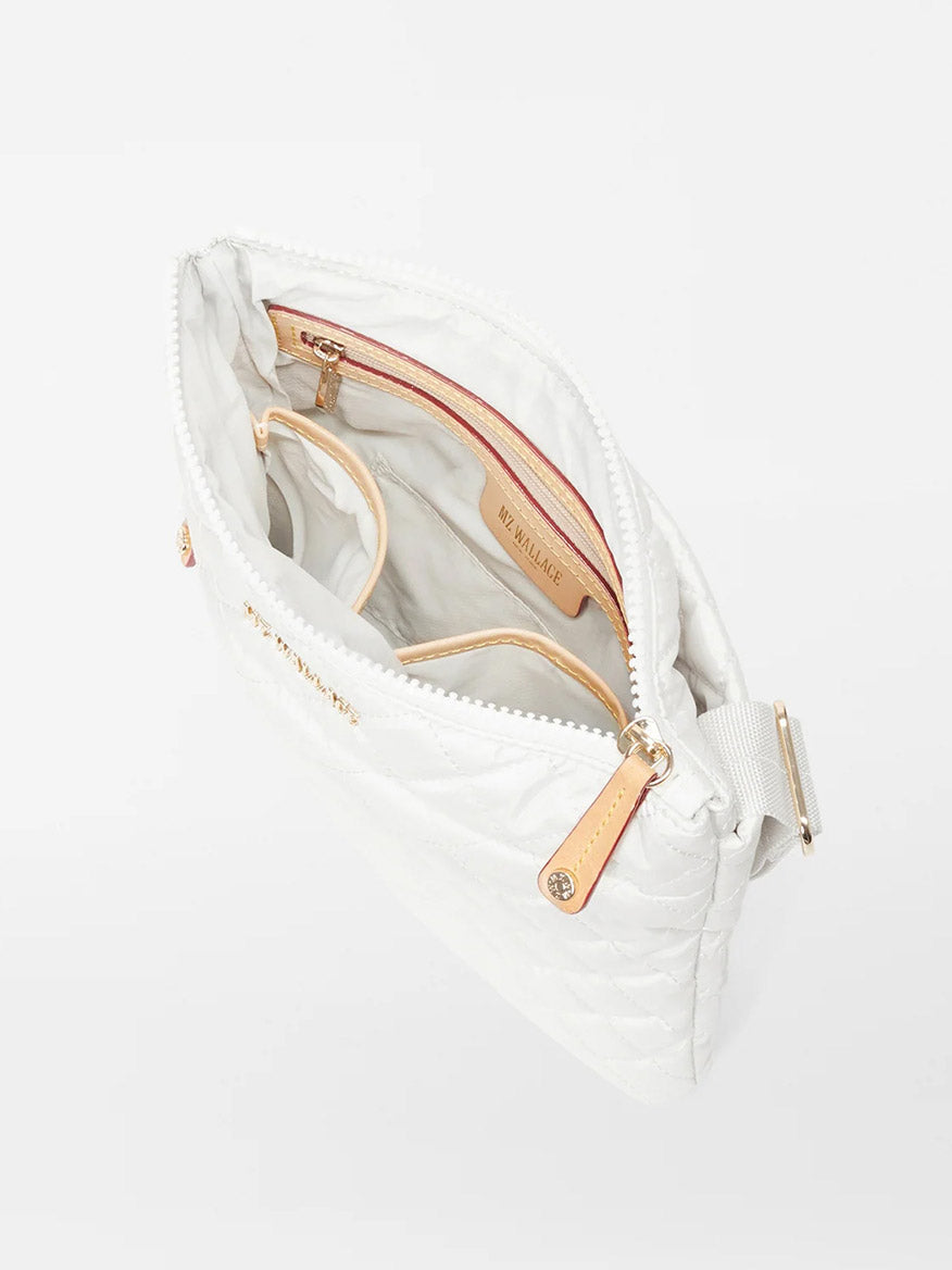 White MZ Wallace Metro Flat Crossbody in Pearl Metallic Oxford open to reveal a beige interior with multiple compartments and gold-tone zippers, viewed from above.