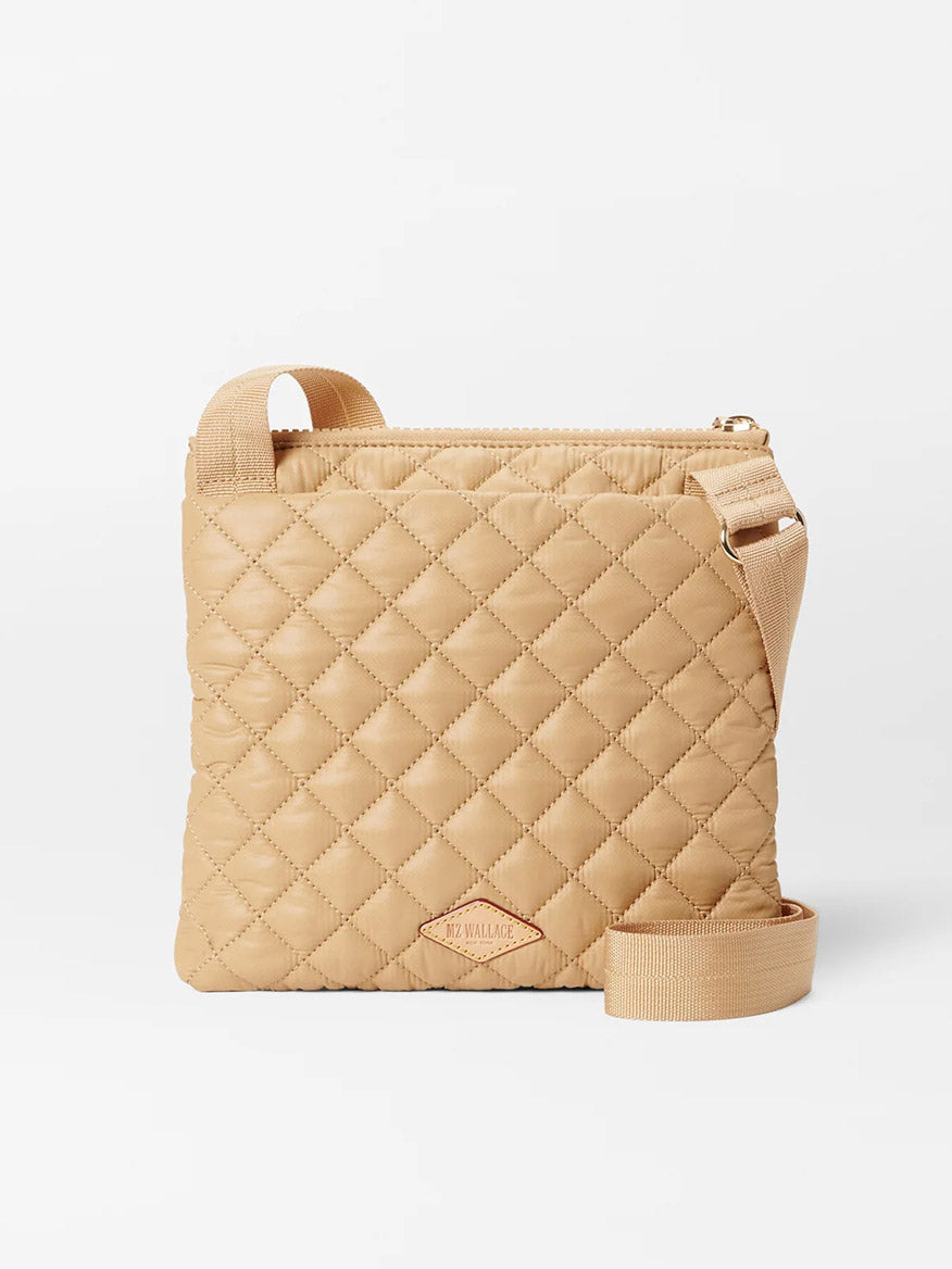 Beige MZ Wallace Metro Flat Crossbody in Camel Oxford with a zipper, featuring a gold-tone brand logo at the bottom center, an adjustable strap, and exterior pockets.