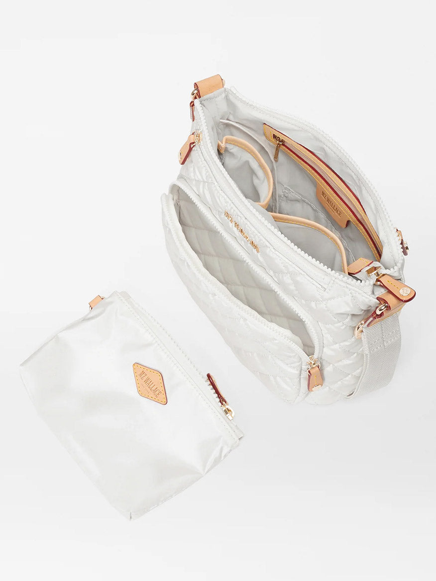 An open MZ Wallace Metro Scout Deluxe in Pearl Metallic Oxford bag with multiple compartments, featuring gold zippers and leather accents, displayed with a matching pouch beside it on a white background.