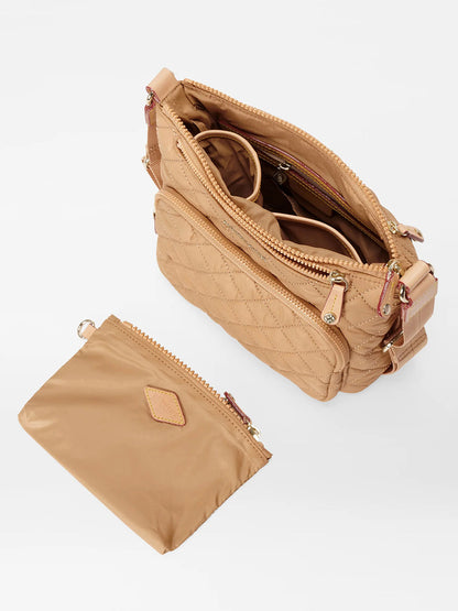 The MZ Wallace Metro Scout Deluxe in Caramel Oxford is a tan quilted crossbody bag made from luxurious Italian leather, with multiple compartments, a zipper closure, and an adjustable strap. It includes a detachable pouch for extra convenience.