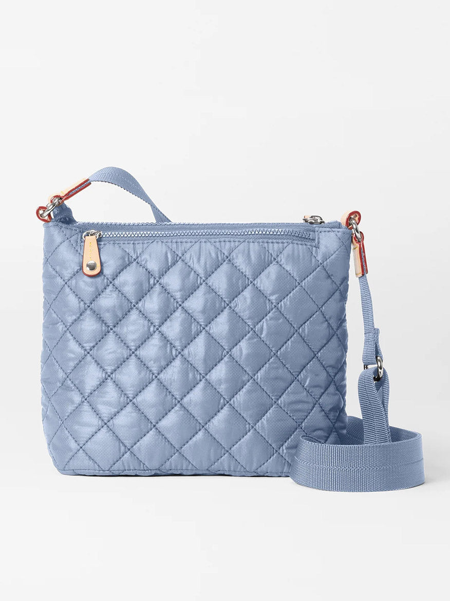 The MZ Wallace Metro Scout Deluxe in Stone Blue Oxford is a quilted crossbody bag with a front zip pocket, adjustable strap, and sleek metallic zippers, embodying timeless elegance.