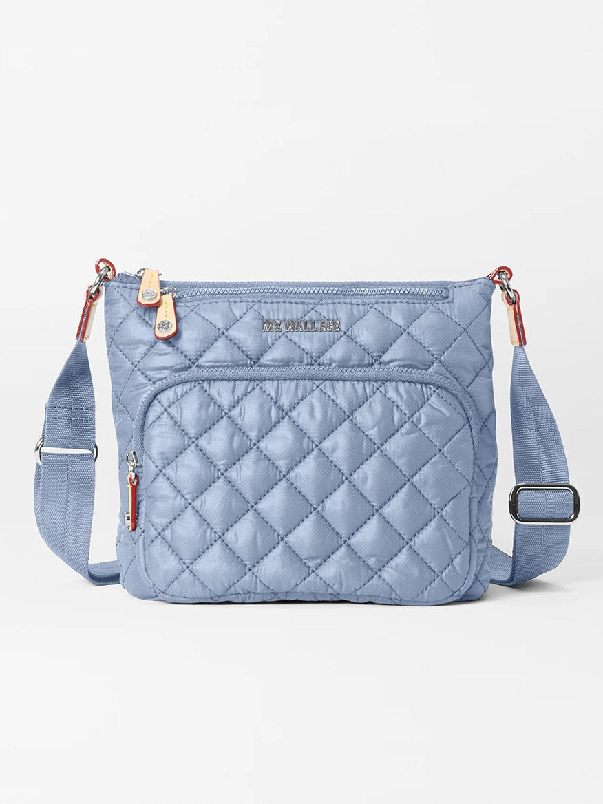 Explore the MZ Wallace Metro Scout Deluxe in Stone Blue Oxford, a graceful quilted crossbody bag made of fine Italian leather. It boasts an adjustable strap, front zip pocket, and a shiny gold-tone brand name plaque for added elegance.