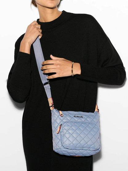 A person in a black outfit holds an MZ Wallace Metro Scout Deluxe quilted shoulder bag in Stone Blue Oxford with a zip pocket.