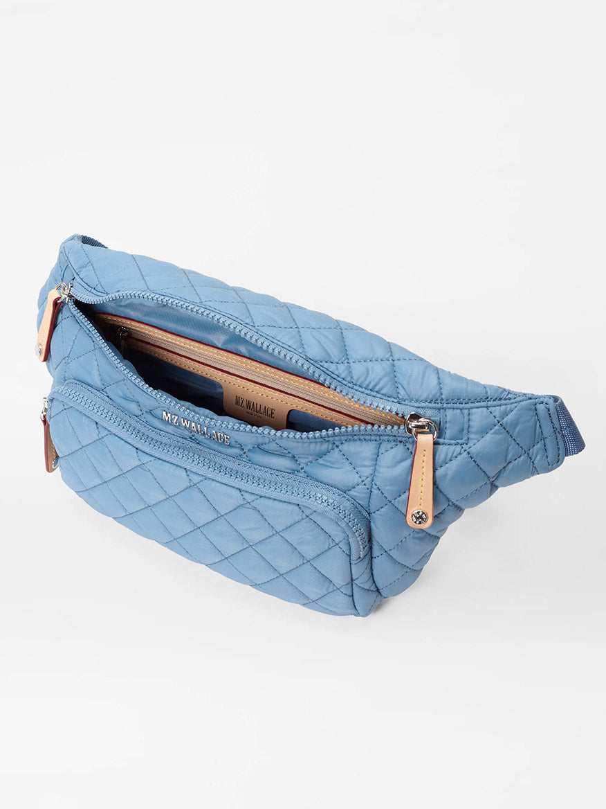 Light blue quilted MZ Wallace Metro Sling in Cornflower Blue Oxford with zipper closure and adjustable waist strap, featuring a logo on the front.