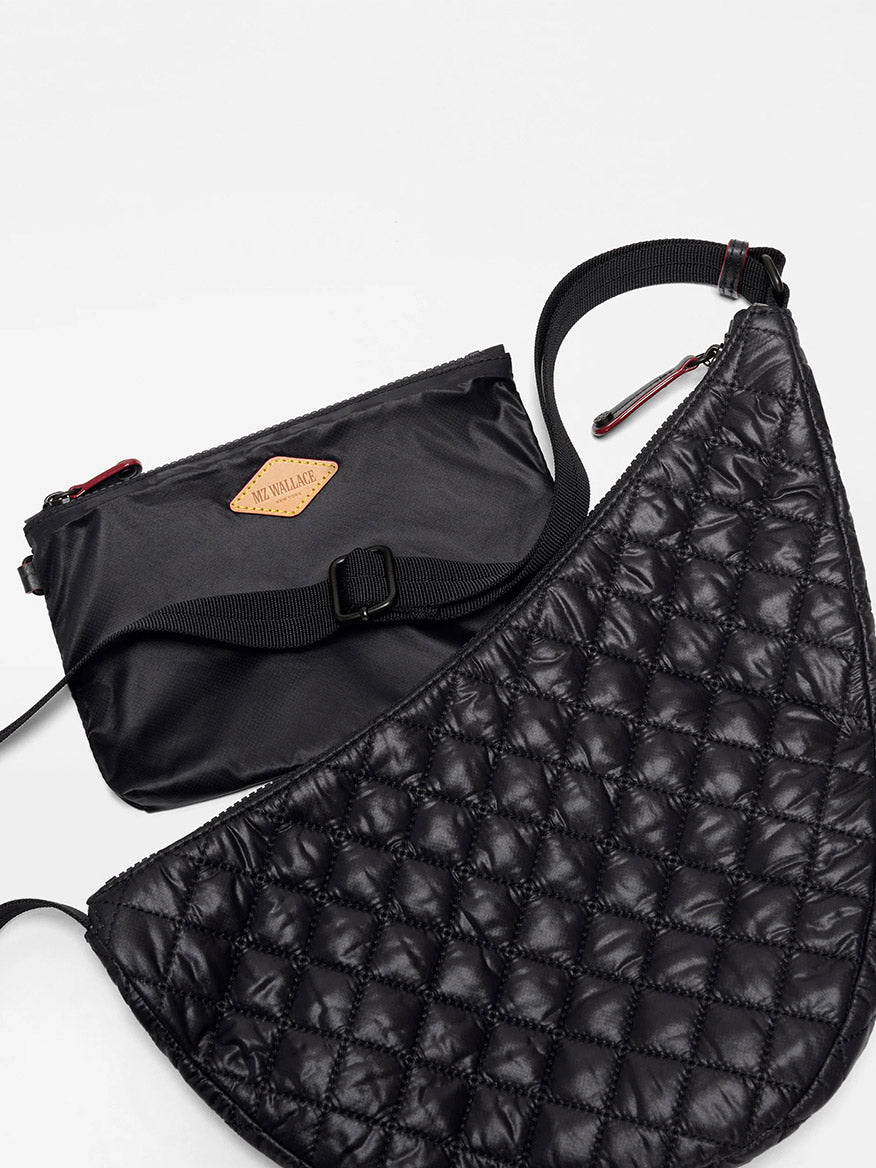 The image shows two black bags: a small, rectangular nylon pouch with a brown logo patch and the MZ Wallace Metro Smile Bag in Black Oxford, which is larger, quilted, curved, and has an adjustable nylon strap.