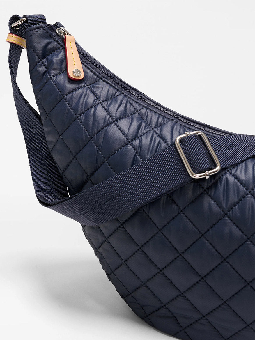 Close-up of the MZ Wallace Metro Smile Bag in Dawn Oxford, featuring quilted navy fabric, Italian leather trim, a navy adjustable nylon strap, zipper closure, and a tan leather zipper pull.