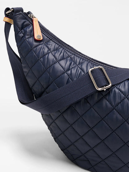 Close-up of the MZ Wallace Metro Smile Bag in Dawn Oxford, featuring quilted navy fabric, Italian leather trim, a navy adjustable nylon strap, zipper closure, and a tan leather zipper pull.