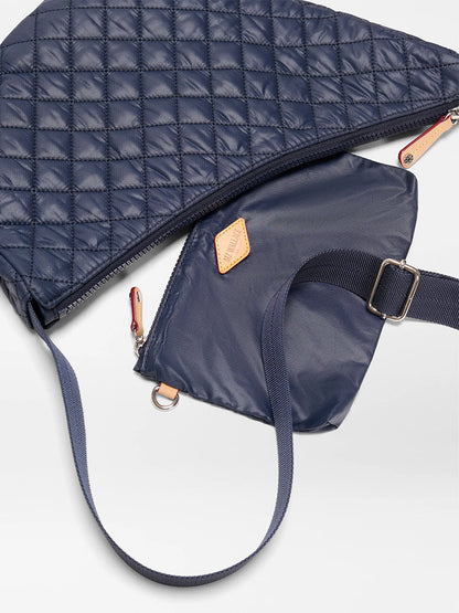 The MZ Wallace Metro Smile Bag in Dawn Oxford is partially open, showing a smaller navy pouch inside with an adjustable nylon strap and a tan patch.
