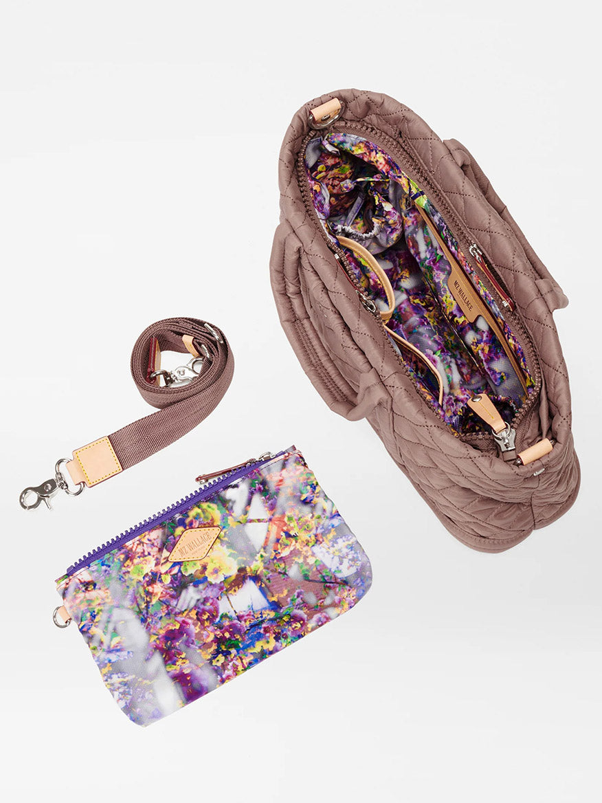 An MZ Wallace Metro Utility Crossbody in Mauve Oxford with an Italian leather trim opened to show a colorful floral lining and a matching floral pouch beside it on a white background.