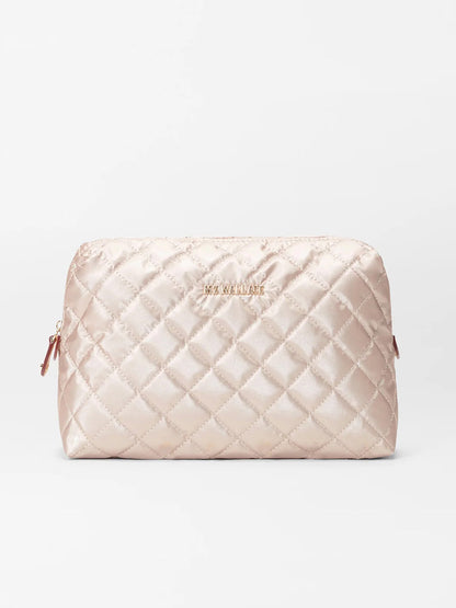 The MZ Wallace Mica Cosmetic in Pale Rose Gold Metallic Oxford is a stunning quilted bag featuring a zipper closure and "MAX MARA" on the front, elegantly combining style and practicality akin to a classic Italian leather dopp kit.