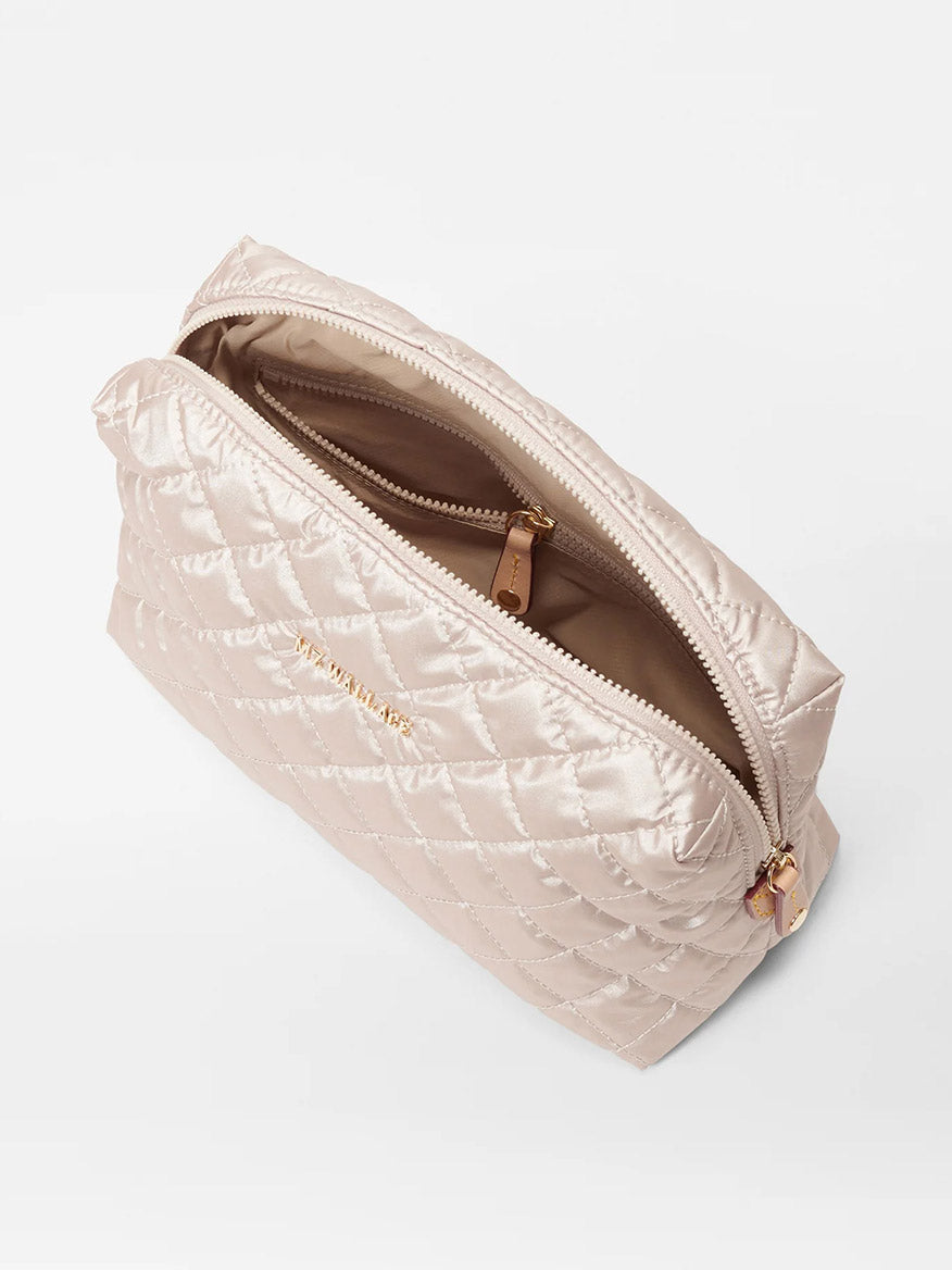 The MZ Wallace Mica Cosmetic in Pale Rose Gold Metallic Oxford features a quilted design with a zipper that opens to reveal a tan interior and gold-toned accents. Expertly crafted from luxurious Italian leather, it serves as the perfect blend of style and function for your cosmetic needs.