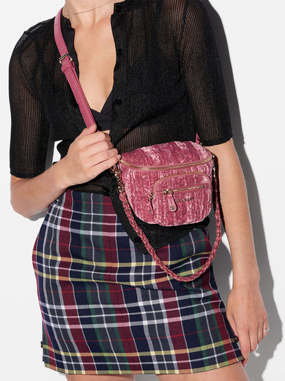 A person wearing a black sheer top, plaid skirt, and holding the MZ Wallace Micro Crosby Crossbody Sling in Petal Velvet.
