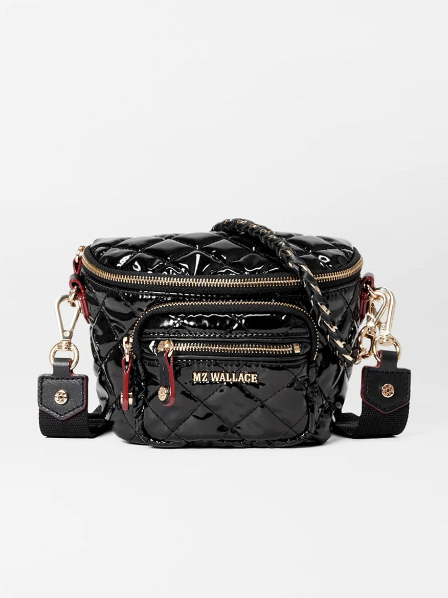 The MZ Wallace Micro Crosby Crossbody Sling in Black Lacquer Oxford is a small, black quilted nylon mini bag featuring gold zippers, a front pocket, elegant Italian leather trim, and two side clasps attached to a woven strap.