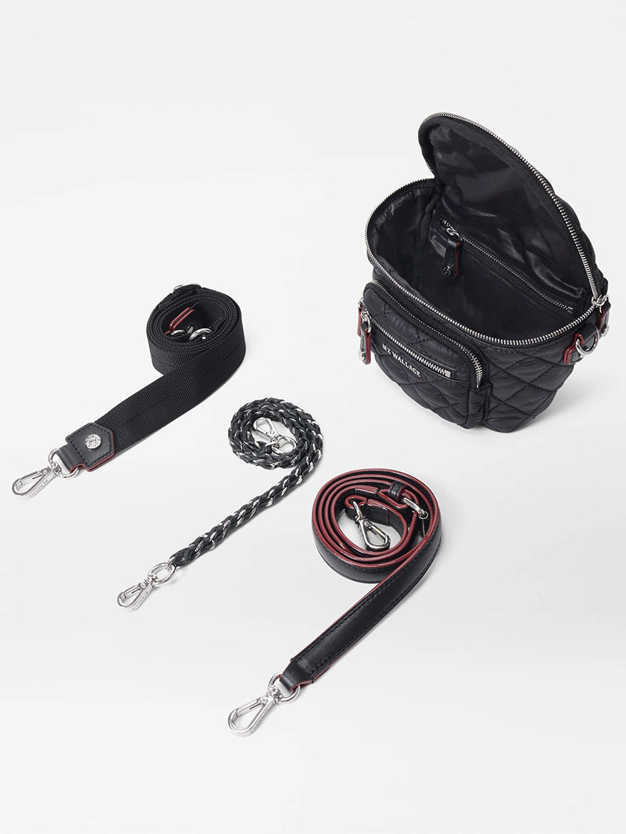 The MZ Wallace Micro Crosby Crossbody Sling in Black Oxford features a sophisticated black quilted design with Italian leather trim and multiple compartments. It comes with three detachable straps: a black fabric strap, a black chain strap, and a black leather strap with red accents. For added security, it includes a zip top closure.