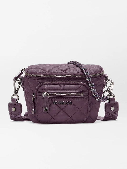 The MZ Wallace Micro Crosby Crossbody Sling in Raisin Oxford is a small quilted purple crossbody bag featuring silver-tone hardware, a front zip pocket, chain and fabric strap, and an “MZ Wallace” logo plaque. Crafted from recycled nylon, this compact sling offers hands-free convenience for carrying your essentials on the go.