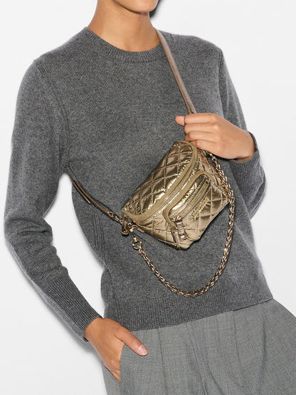 Person wearing a gray sweater and holding the MZ Wallace Micro Crosby Crossbody Sling in Antique Gold Metallic Oxford, a quilted metallic crossbody bag with a chain strap featuring elegant gold hardware.