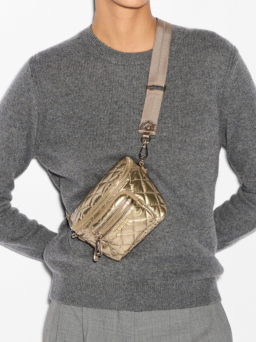 Person wearing a gray sweater and pants with the MZ Wallace Micro Crosby Crossbody Sling in Antique Gold Metallic Oxford, showcasing elegant Italian leather and gleaming gold hardware.